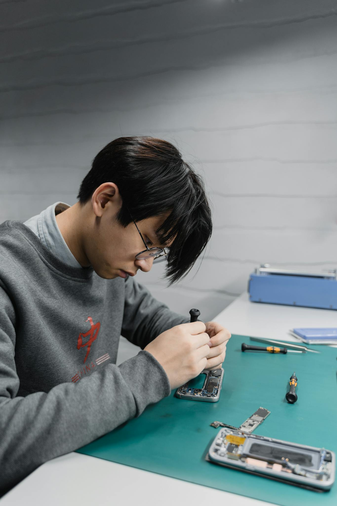 Focused young technician repairing a smartphone indoors at a workstation.