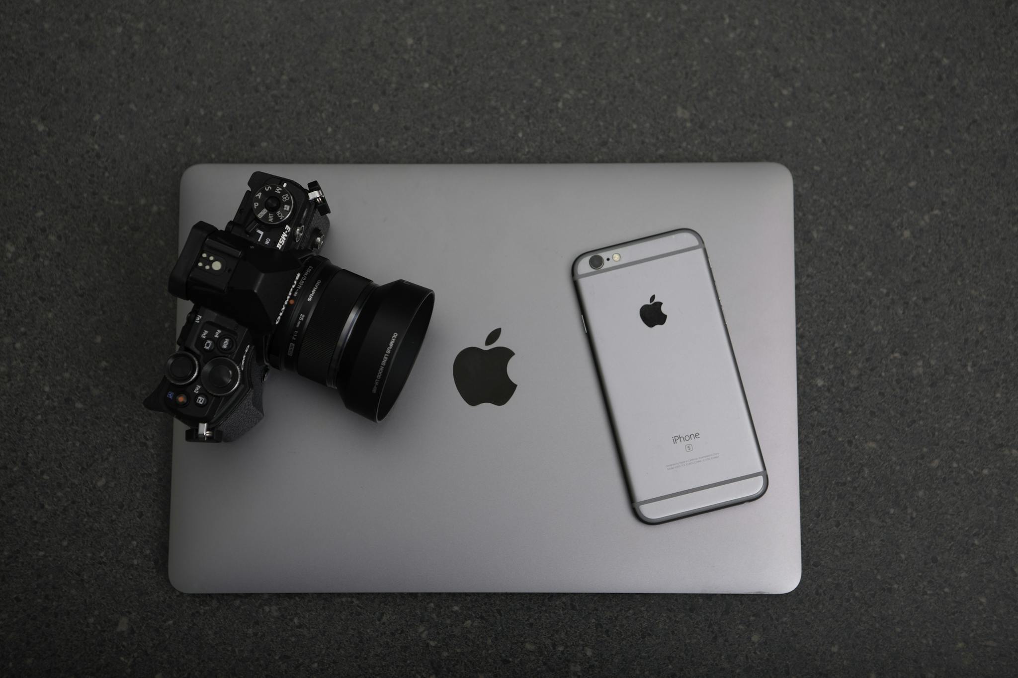High-angle shot of DSLR camera, MacBook, and iPhone on textured surface, showcasing modern technology essentials.