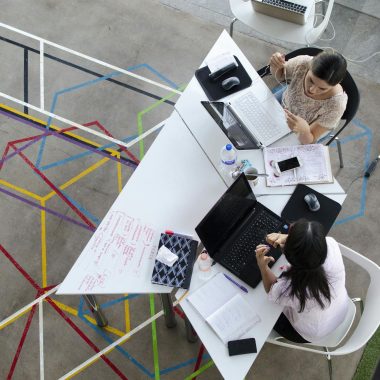 Overhead view of women working together in a modern office setting with colorful geometric floor design.